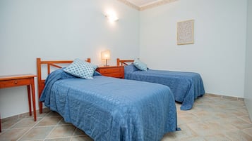 A room with two beds, a nightstand, a lamp, and a small table.