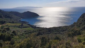 Un paisaje costero con vista despejada al mar, terreno montañoso y una cadena de montañas distante.