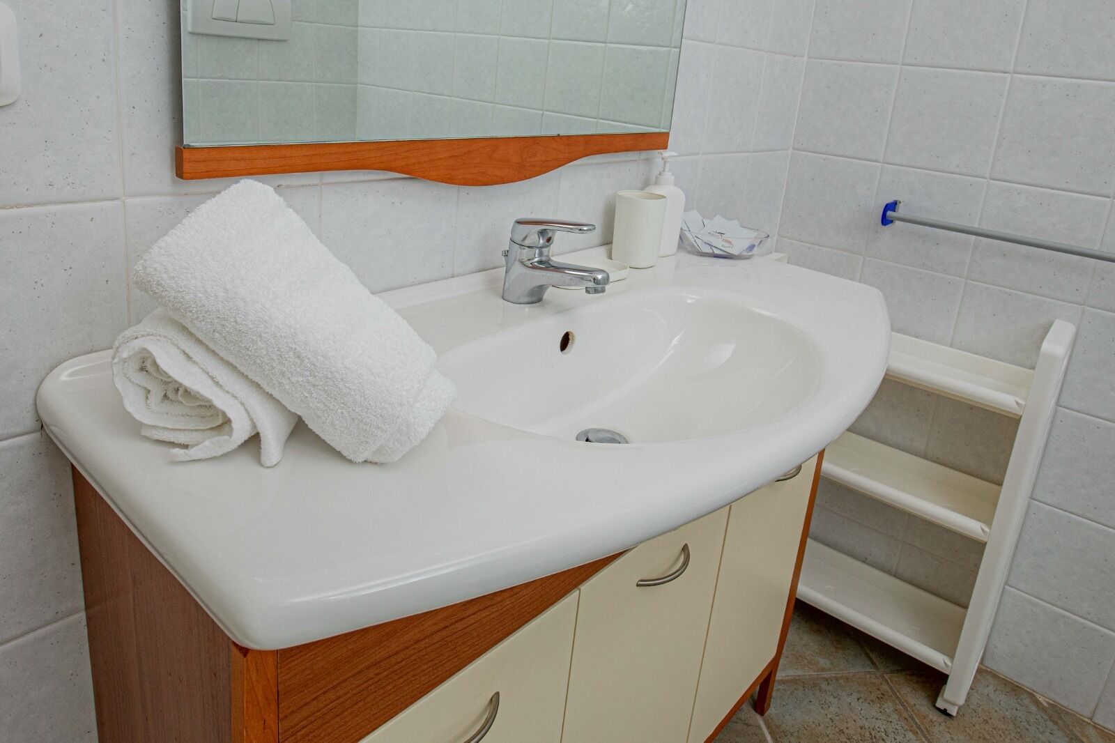 A bathroom with a white sink, a mirror, a towel, and a soap dispenser.