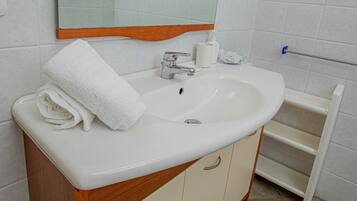 A bathroom with a white sink, a mirror, a towel, and a soap dispenser.