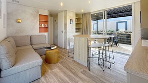 Un soggiorno moderno con un divano, un tavolino e un angolo bar con sgabelli. Una porta vetrata scorrevole dà accesso a un patio esterno.