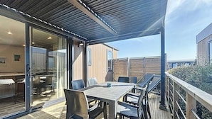 Patio esterno con pavimento in legno, tavolo e sedie, e una porta vetrata che dà su un ambiente interno.