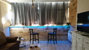 A living room with a wooden bench, two chairs, a TV, and a window with curtains.