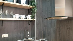 A modern kitchen with a stainless steel sink, wooden shelves, and a black range hood.