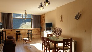 A cozy living room with a wooden floor, a dining table with chairs, a sofa, and a TV.