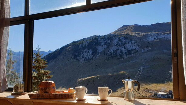A wooden table with a loaf of bread, a jar of pickles, and a coffee maker.