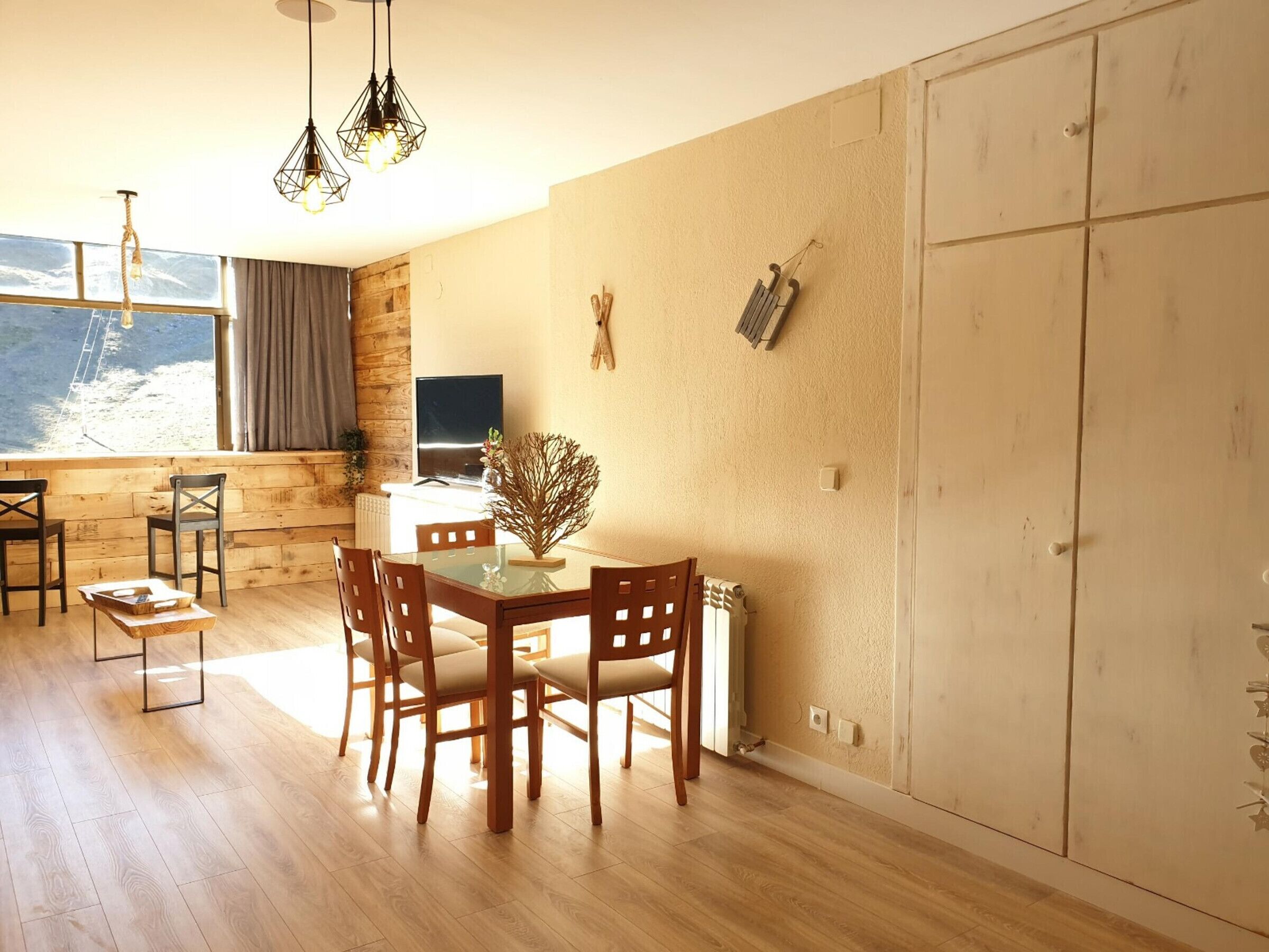 Un comedor con una mesa y sillas de madera, un televisor y vistas al exterior.