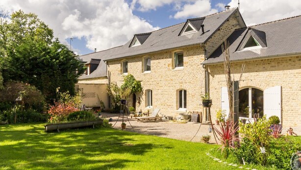 A stone building with a sloped roof, a garden with a lawn, and outdoor seating.