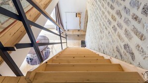 A wooden staircase leading to a room with a stone wall and a ceiling light fixture.