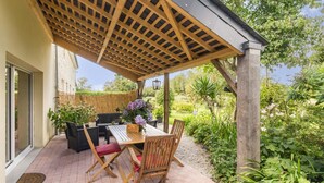 An outdoor patio with a wooden pergola, a table, and chairs.