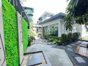 A modern building with a green vertical garden, a pathway with stepping stones, and a variety of potted plants.