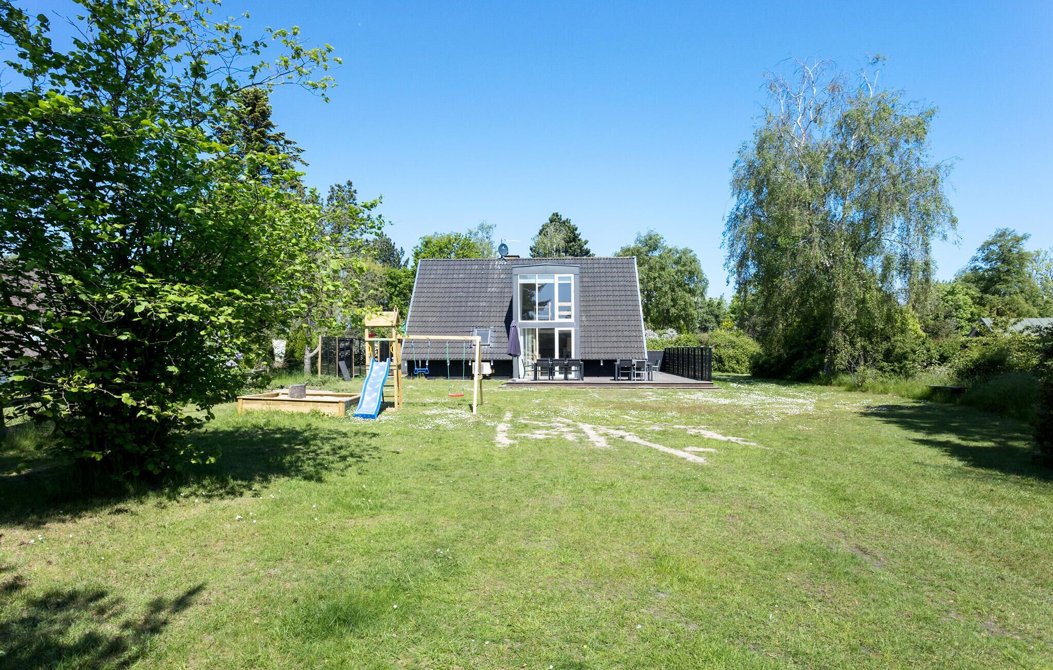 Ett hus med en stor veranda, en gunga och en rutschkana på gården.