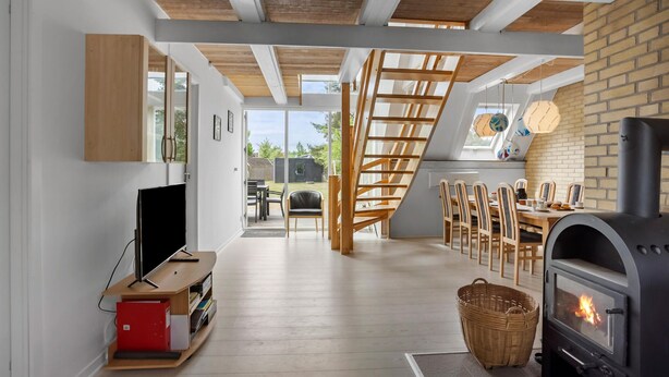 Un intérieur moderne avec un escalier en bois, un coin repas avec des chaises, un téléviseur et une cheminée.