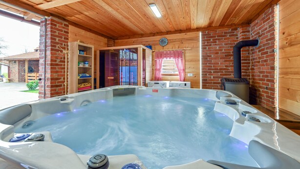 A hot tub in a wooden cabin with a brick wall, a window with red curtains, and a fireplace.