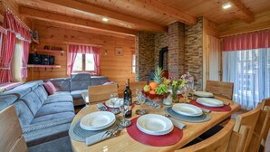A wooden cabin interior with a dining table set for four, a sofa, and a kitchen area with a brick wall and wooden ceiling.