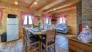 A cozy cabin-style room with a dining table, chairs, a sofa, a refrigerator, and a brick fireplace.