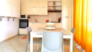 A modern kitchen with white cabinets, a microwave, stove, and a sink. There is a dining table with chairs and a yellow curtain.
