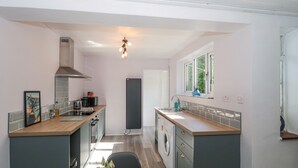 A modern kitchen with a central island, a built-in oven, a dishwasher, and a window providing natural light. - Stones Throw (Lymington)