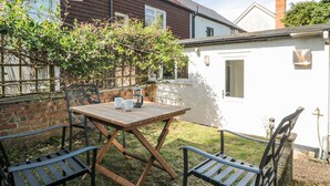A wooden table with two chairs in a garden area with a brick wall and a white building in the background. - Stones Throw (Lymington)
