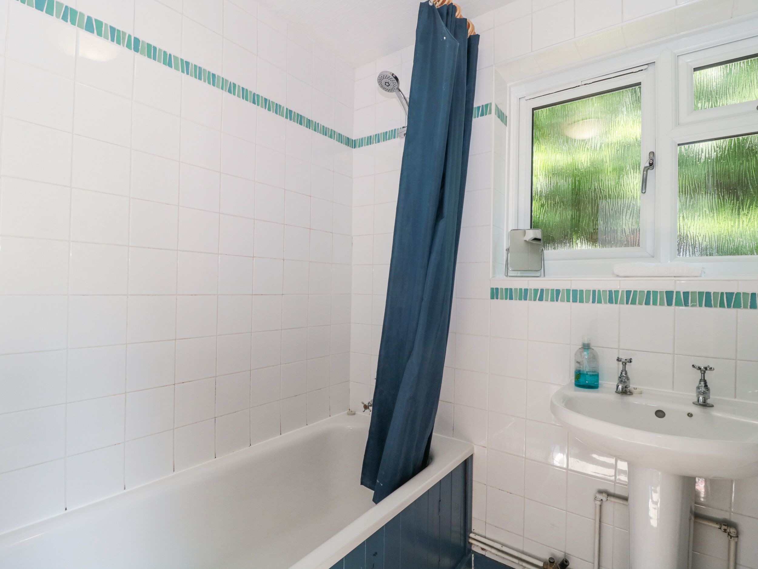 A bathroom with a bathtub, a sink, and a window with a view of greenery.