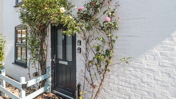 A white brick building with a black door and a small window. - Stones Throw (Lymington)