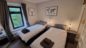 Une chambre avec deux lits, une fenêtre avec des rideaux, un radiateur et une œuvre d’art représentant une carte du monde accrochée au mur.