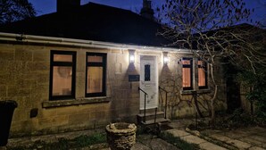 Un bâtiment en pierre avec une porte et des fenêtres blanches, un petit porche et un jardinière en pierre au premier plan.