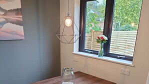 Une table en bois avec un banc, un luminaire suspendu et une fenêtre donnant sur un paysage verdoyant.