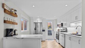 A modern kitchen with white cabinetry, a central island, stainless steel appliances, and a breakfast bar. - Signal Hill Elegance 3Bd A/C Hiking (St. John's)