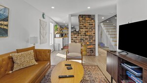 A modern living room with a leather sofa, a coffee table, a TV, and a kitchen in the background. - Queen Top Suite 2BR Free Parking Modern (St. John's)