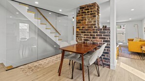 A modern interior with a wooden dining table, grey chairs, a brick accent wall, and a glass partition with a staircase. - Queen Top Suite 2BR Free Parking Modern (St. John's)