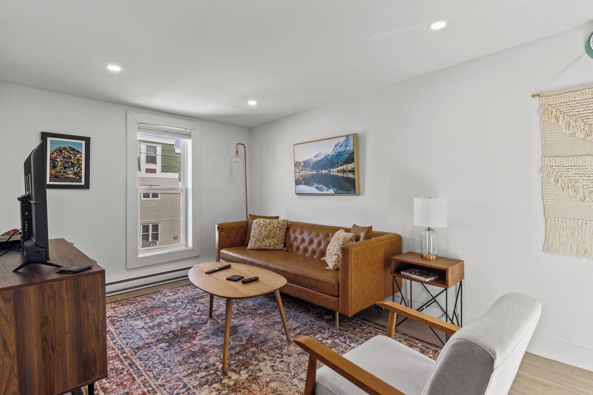 A modern living room with a brown sofa, a wooden coffee table, a white armchair, and a small side table with a lamp.