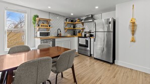 A modern kitchen with white tiled walls, wooden shelves, a stainless steel refrigerator, and a dining area with a wooden table and chairs. - Queen Top Suite 2BR Free Parking Modern (St. John's)