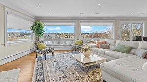 A spacious living room with a large window, a white sofa, a coffee table, and a patterned rug.