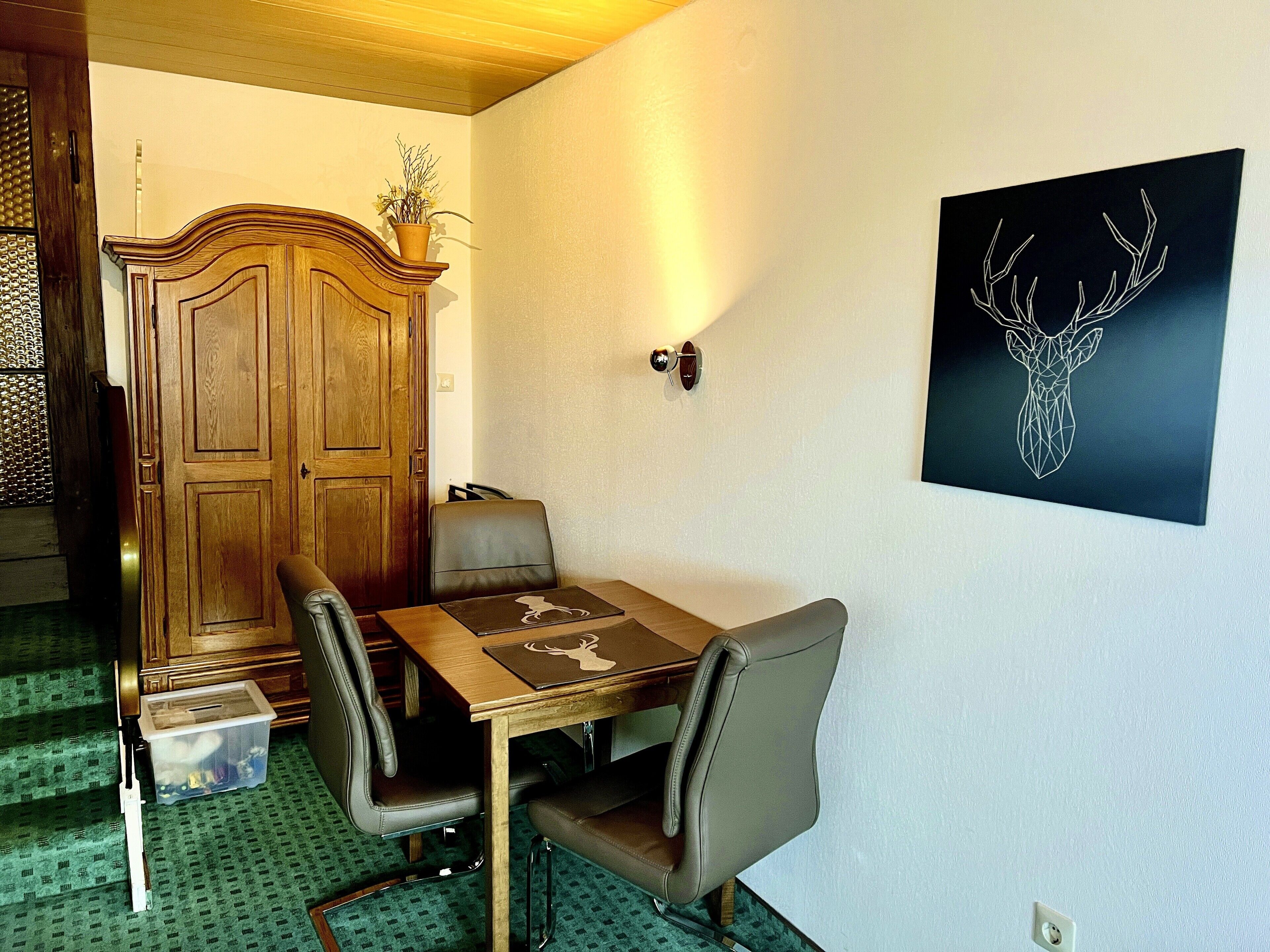 A dining area with a wooden table, leather chairs, a wooden cabinet, and a wall-mounted deer head artwork.