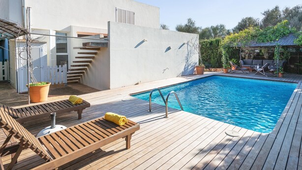 A swimming pool with wooden deck loungers and a white building with a staircase.