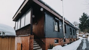 Uma casa de dois andares com fachada de tijolos, janelas amplas e varanda coberta.