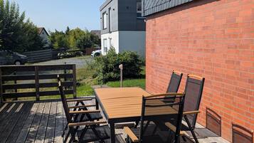 Eine Terrasse im Freien mit einem Holztisch und -stühlen, einer Ziegelwand und einem modernen Gebäude im Hintergrund.
