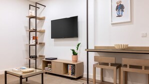 A modern living room with a flat-screen TV mounted on the wall, a wooden coffee table, a bookshelf, and a dining area with a table and chairs. - Fervença Boutique Palace 1 by HostWise (Vila Nova de Gaia)