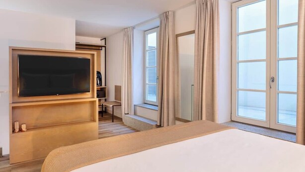 A hotel room with a large bed, a TV, a desk, and a window with curtains. - Fervença Boutique Palace 1 by HostWise (Vila Nova de Gaia)