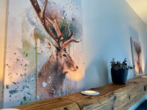 A wall with a painting of a deer, a wooden bench, and a potted plant.