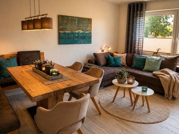 Un salon chaleureux avec une table à manger en bois, deux canapés, une table basse et une grande fenêtre avec des rideaux.