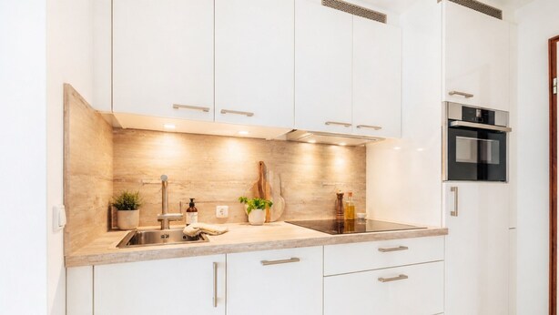 Una cocina moderna con armarios blancos, un lavamanos de acero inoxidable y un horno empotrado.