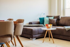 Ein modernes Wohnzimmer mit einem braunen Ledersofa, einem runden Holztisch mit Obstschale und einer Lampe.