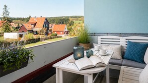 Un balcón con una mesa blanca, un sofá y vistas a casas al fondo.