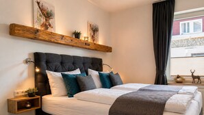Un dormitorio con una cama grande, mesitas de noche, un aparador, una ventana con cortinas y decoración en la pared.