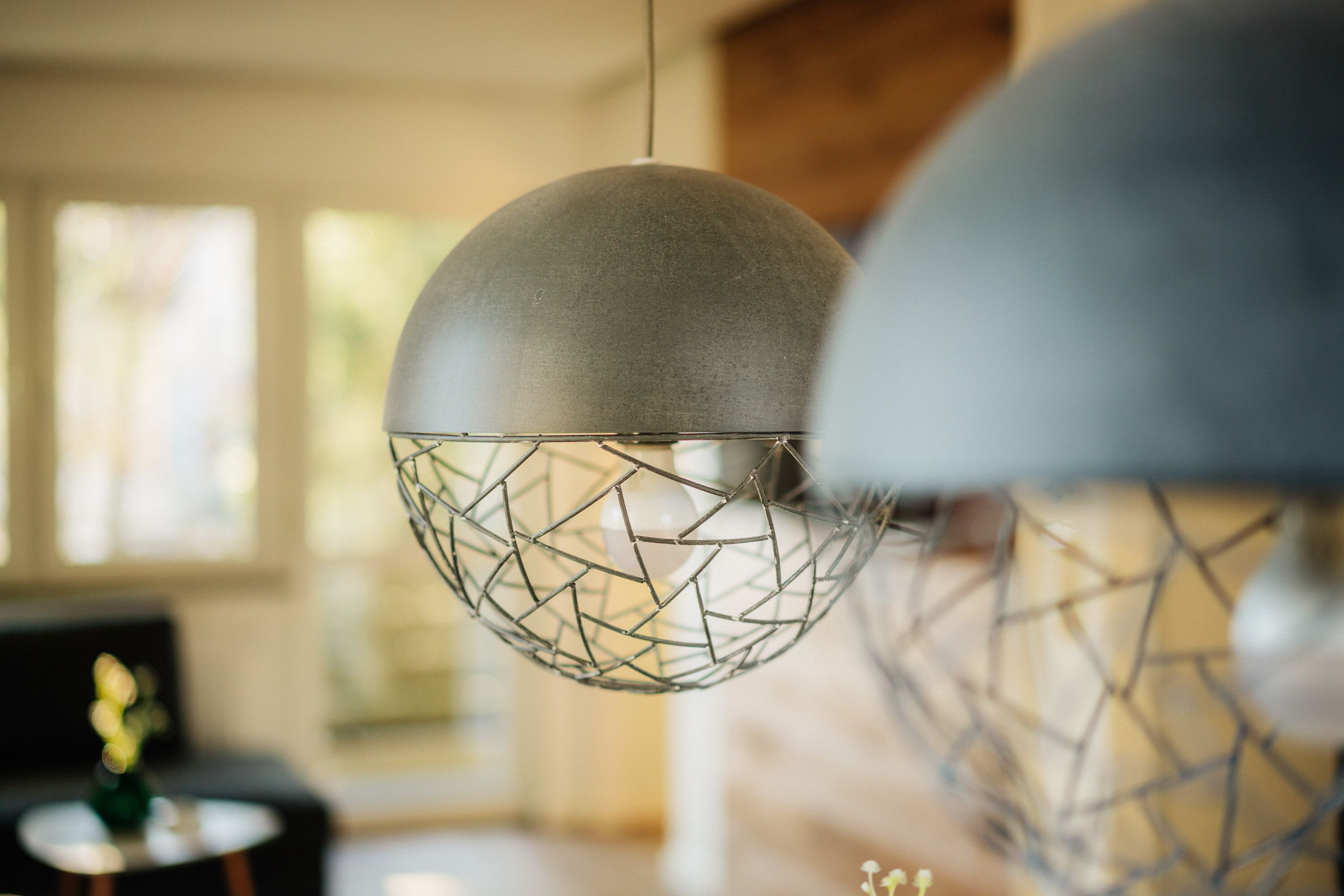 Zwei kugelförmige Pendelleuchten mit geometrischem Drahtdesign, die in einem gut beleuchteten Raum mit modernem Interieur hängen.