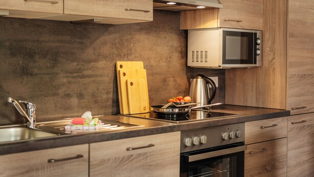 A modern kitchen with wooden cabinets, a stainless steel sink, a microwave, and a stove.