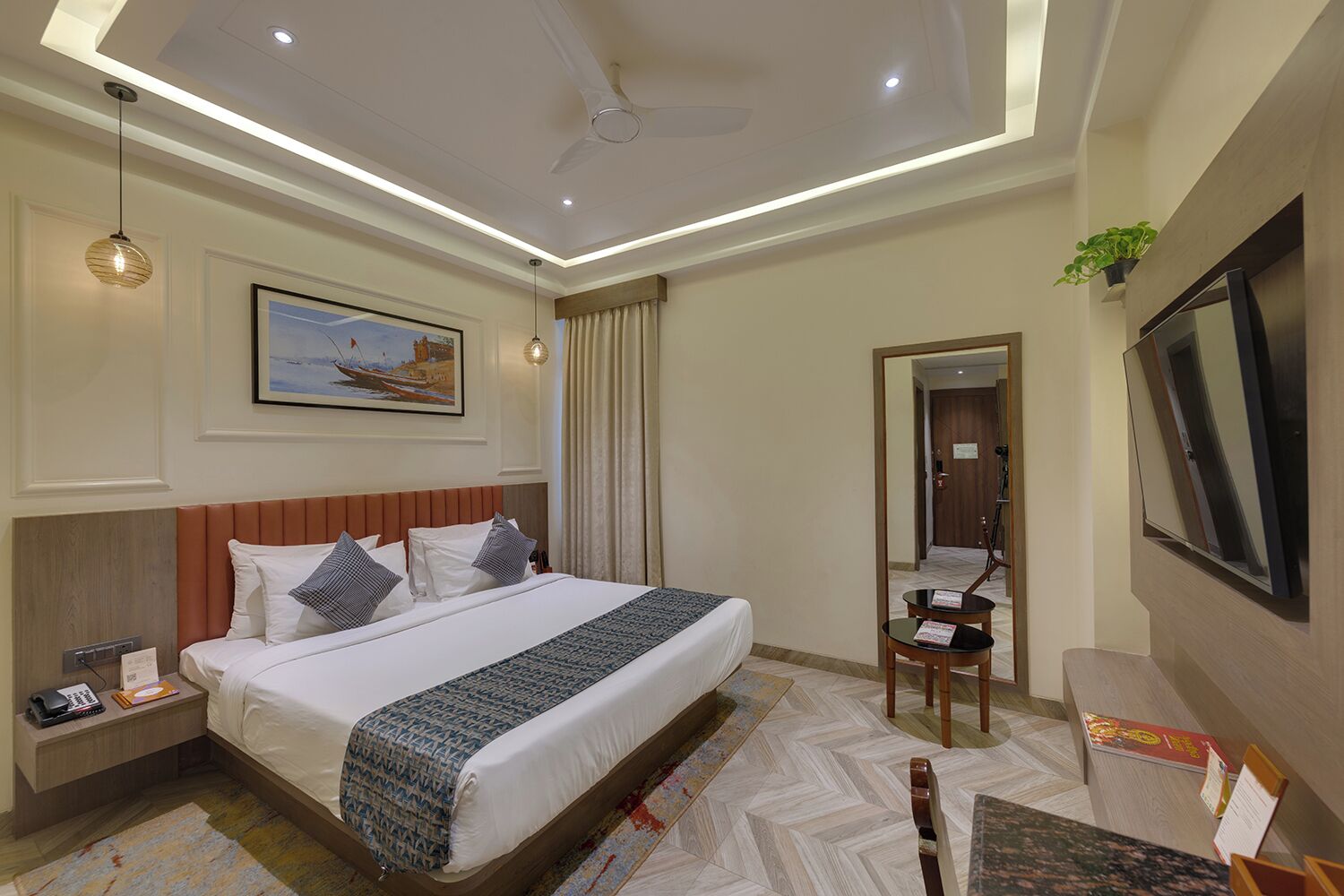 A hotel room with a bed, bedside table, lamp, TV, and a painting on the wall.