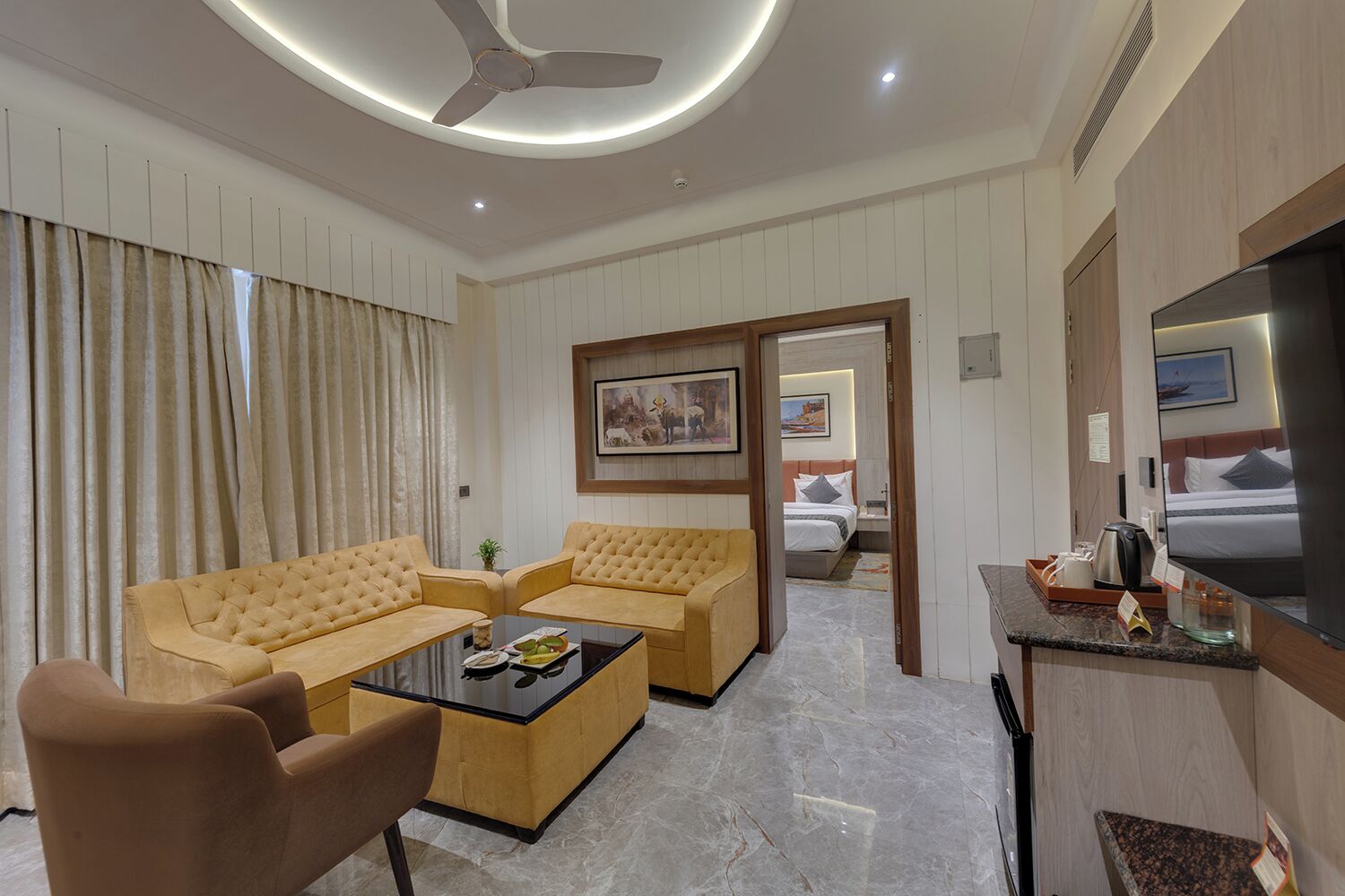 A hotel room with a sofa set, a coffee table, a TV, and a bed with a nightstand.
